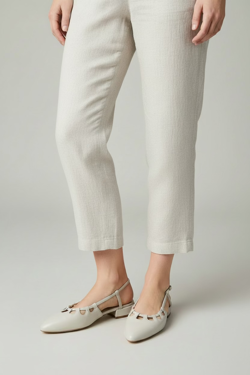 A pair of almond pointed-toe slingback flats with cutout detailing across the instep, displayed on a round woven rattan table in front of a dark blue office cabinet.
