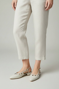 A pair of almond pointed-toe slingback flats with cutout detailing across the instep, displayed on a round woven rattan table in front of a dark blue office cabinet.